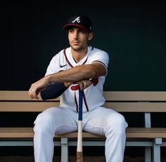 a baseball player sitting on a bench with a bat in his hand and wearing a uniform