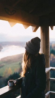 a woman standing on top of a balcony next to a cup of coffee and looking at the ocean