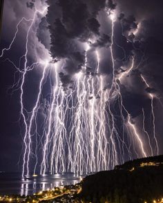 lightning strikes over the ocean and city lights