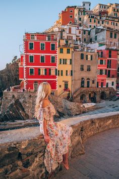 a woman is standing on the edge of a wall looking out at buildings and cliffs