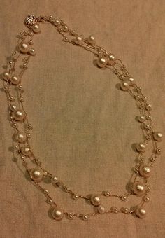 a necklace with pearls and silver beads on a tan cloth background is seen in this image