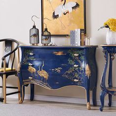 two chairs and a blue dresser with birds on it in front of a yellow painting