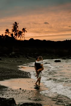 a man carrying a woman on his back while walking along the beach at sunset with palm trees in the background