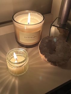 two candles sitting on top of a table next to a rock and glass jar filled with liquid