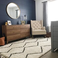 a living room with a chair, dresser and mirror on the wall next to a window