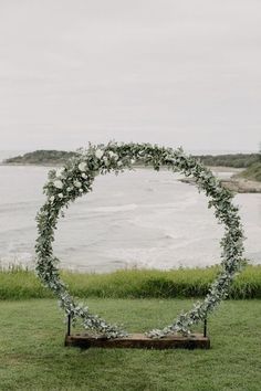 a wedding arch with flowers and greenery on the grass by the water in front of an ocean