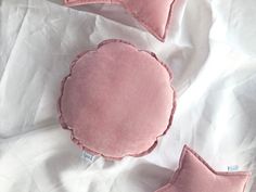 three pink pillows are laying on a white sheet with one pillow in the shape of a flower