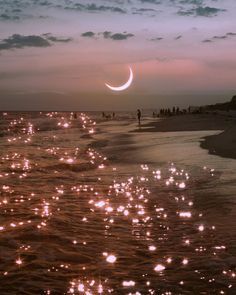 the moon is reflected in the water as people walk on the beach