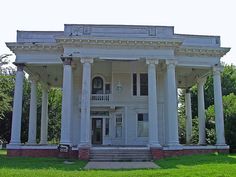 an old white house with columns and pillars on the front porch, in a grassy area