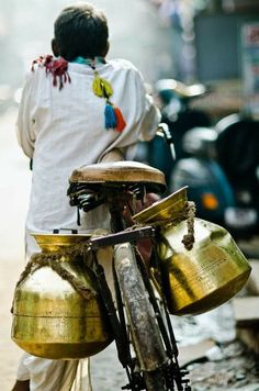 a man walking down the street next to a bike with bells on it's back