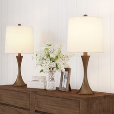 two lamps sitting on top of a dresser next to a vase with flowers in it