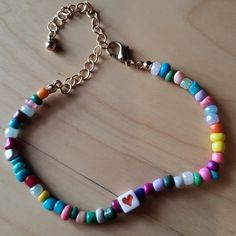 a multicolored beaded bracelet with a heart charm hanging from the clasp on a wooden table