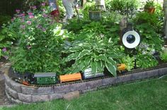 a toy train set in the middle of a garden with lots of plants and flowers