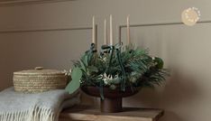 a wooden table topped with a vase filled with greenery and candles next to a blanket