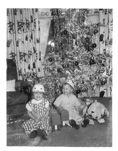 two young children sitting in front of a christmas tree with stuffed animals on the floor