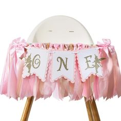 a pink and gold 1st birthday party decoration on a chair with ruffled ribbon around the legs