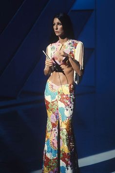 a woman standing in front of a microphone wearing a colorful skirt and cropped top