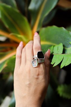 a woman's hand with a ring on it and a green plant behind her