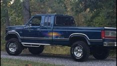 a blue pick up truck parked on the side of a road in front of trees