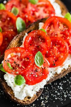 two pieces of bread with tomatoes and cheese on them, sitting on a black plate