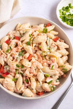 a white bowl filled with pasta salad next to a fork and knife on a table