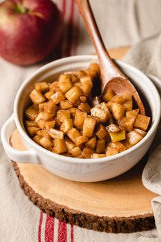 a bowl filled with food sitting on top of a wooden cutting board next to an apple