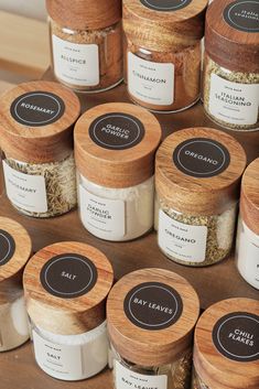 many jars with different types of spices on top of a wooden table next to each other