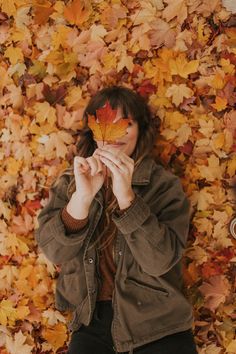 a woman sitting in front of a pile of leaves holding a leaf up to her mouth