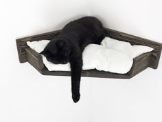 a black cat laying on top of a white pillow in a wooden shelf with pillows