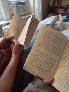 a person laying in bed reading a book with their hands on top of each other