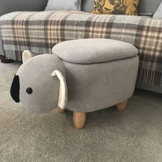 a grey elephant stool sitting on top of a carpeted floor next to a couch