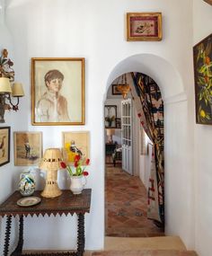 a hallway with pictures and paintings on the wall next to a table in front of a doorway