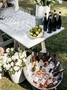 a table with wine glasses, bottles and flowers on it in the middle of grass