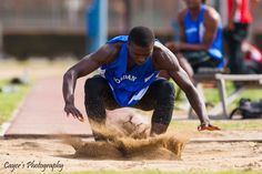 a man in blue shirt and black pants playing in sand on a track with other people behind him