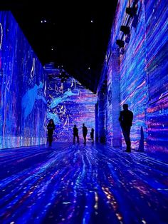 people are walking through an art installation with blue lights on the walls and in the floor