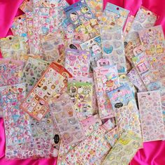 many different types of stickers on a pink cloth covered bed sheet with the words hello kitty printed on them