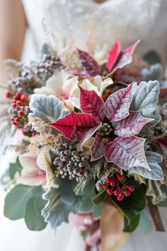 a bridal bouquet with red, white and green flowers in the center is held by a bride's hand