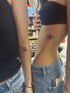 two women with tattoos on their stomachs are standing next to each other in jeans