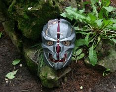 a helmet that is sitting on the ground next to some rocks and plants with leaves around it