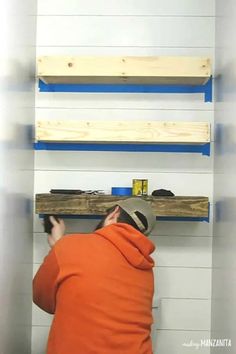 a man in an orange hoodie is working on some shelves with blue paint and wood planks