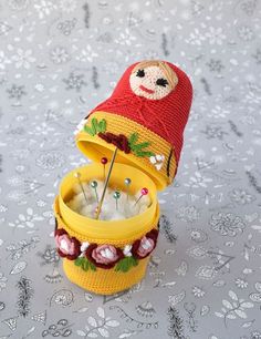 a knitted hat sitting on top of a yellow container filled with pins and needles