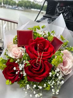 a bouquet of red and pink roses sitting on top of a table next to water