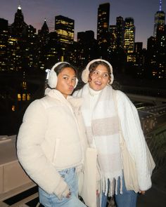 two women standing next to each other in front of a cityscape at night