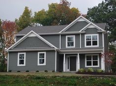 a gray house with white windows and trees in the background