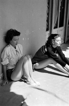 two women sitting on the ground next to each other in front of a door and window