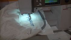 the sewing machine is being used to sew on white fabric with blue lettering underneath