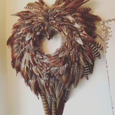 an animal's head made out of feathers on a white wall with a hole in the middle