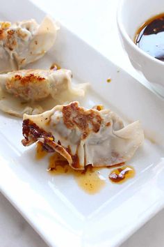 some dumplings are sitting on a white plate next to a bowl of dipping sauce