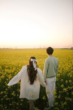 a man and woman standing in a field holding hands