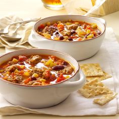 two white bowls filled with chili and cornbread crackers on top of a table